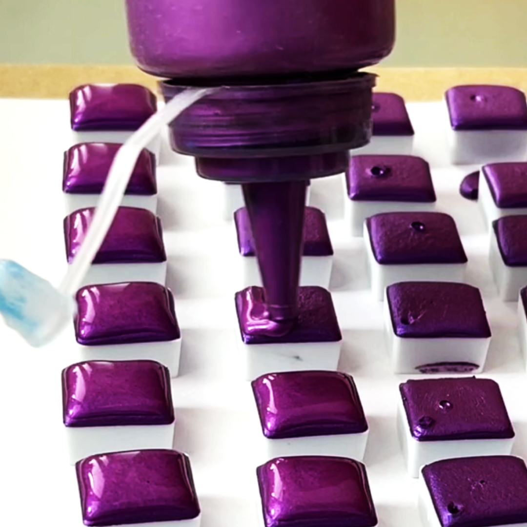 Dispensing rich purple liquid watercolor pigment into half-pans during production process by VHacademy
