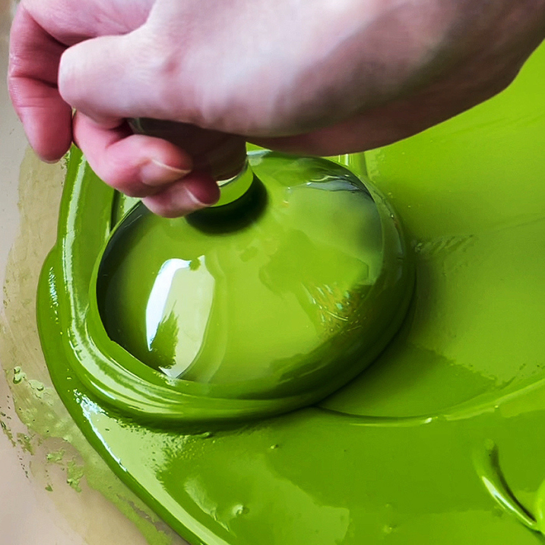 Handheld muller blending glossy lime green liquid pigment paste on glass slab by VHacademy